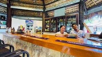 A bar area with a wooden counter, bar stools, and a thatched roof ceiling.
