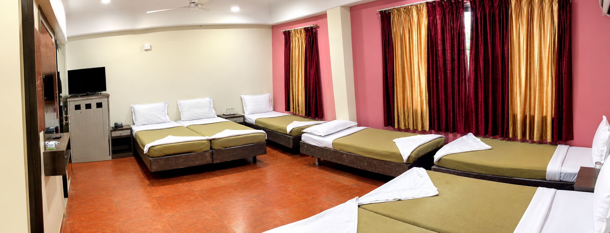 A hotel room with four single beds, a desk with a flat-screen TV, and a minibar.