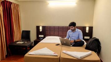 A hotel room with a bed, a desk, a chair, a laptop, and a suitcase.