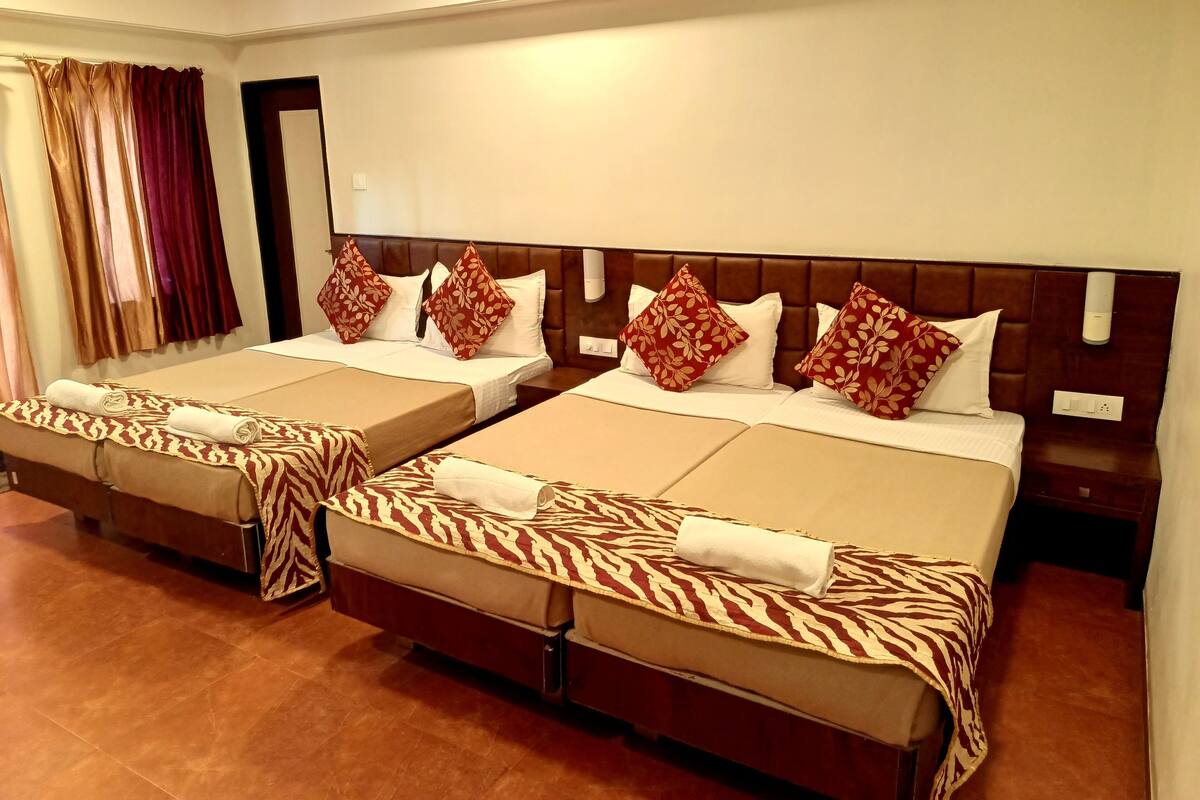 Habitación de hotel con dos camas, cada una con cabecero, y un ventanal grande con cortinas.