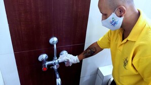 A person in a yellow shirt operating a shower control valve in a bathroom with dark brown tiles. - Hotel Viva Baga (Baga)