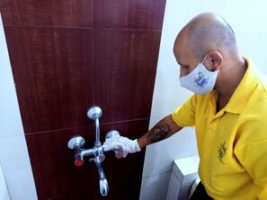 A person in a yellow shirt operating a shower control valve in a bathroom with dark brown tiles. - Hotel Viva Baga (Baga)