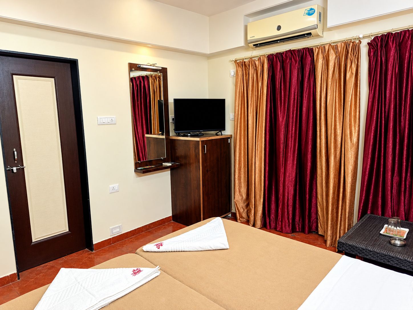 Habitación de hotel con cama, televisor, espejo y ventana con cortinas.