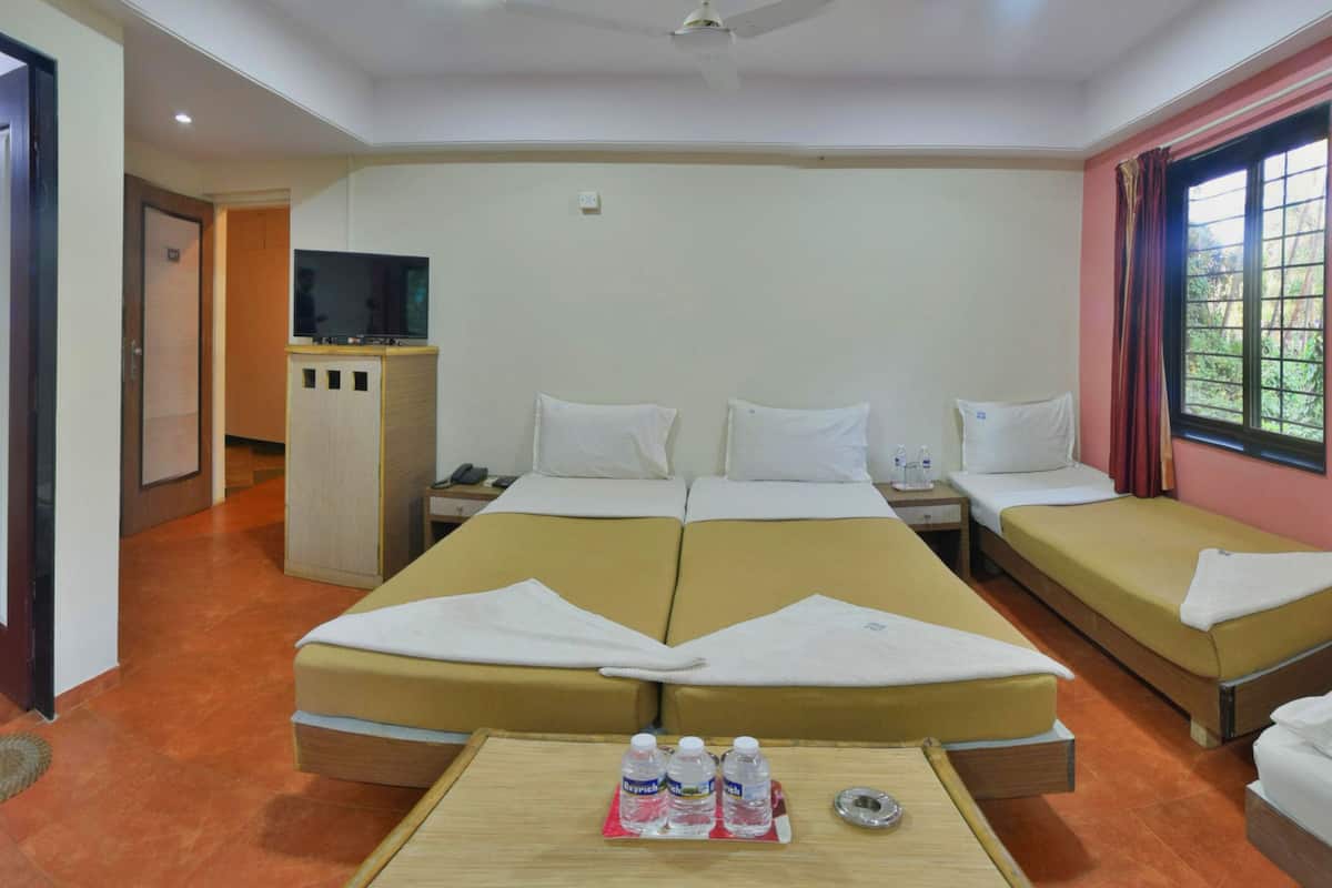 Habitación de hotel con dos camas individuales, un sofá cama, televisión, escritorio pequeño y ventana con cortinas.