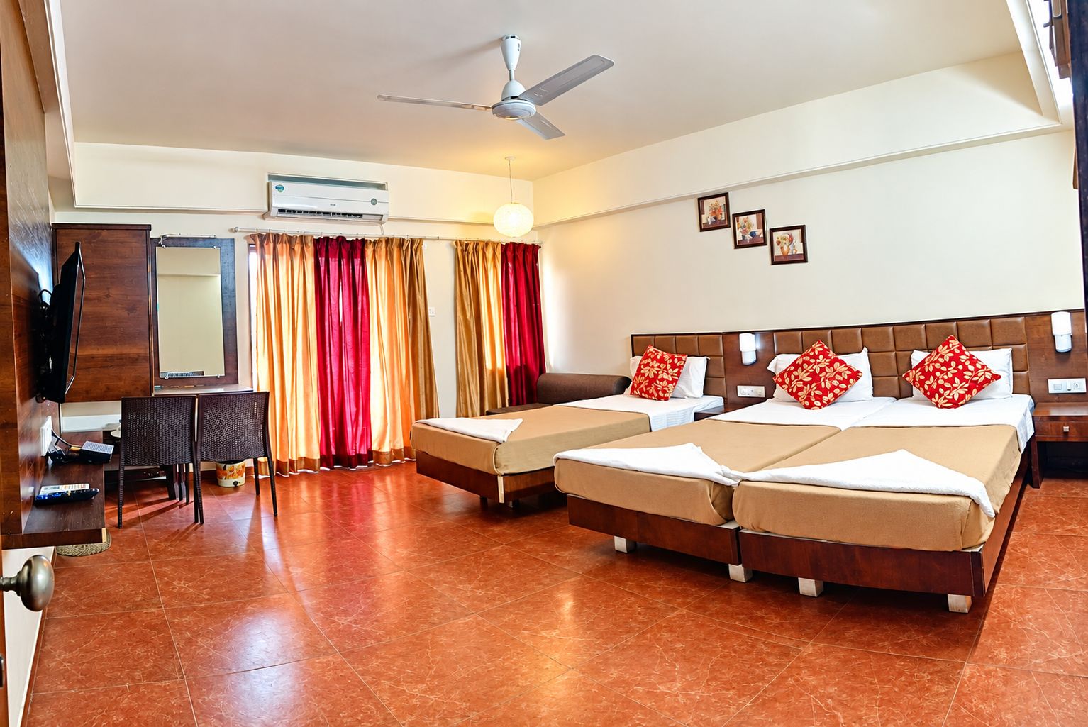 A hotel room with two beds, a desk, a chair, an air conditioning unit, and a ceiling fan.