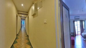 A hotel hallway with patterned floor tiles, a door with a frosted glass panel, and a bed with a red headboard in the adjacent room. - Hotel Viva Baga (Baga)