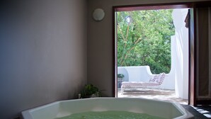 Uma área de spa com uma banheira de hidromassagem, uma espreguiçadeira e vista para um jardim.