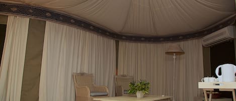 A tented room with a table, chairs, a lamp, and a potted plant.
