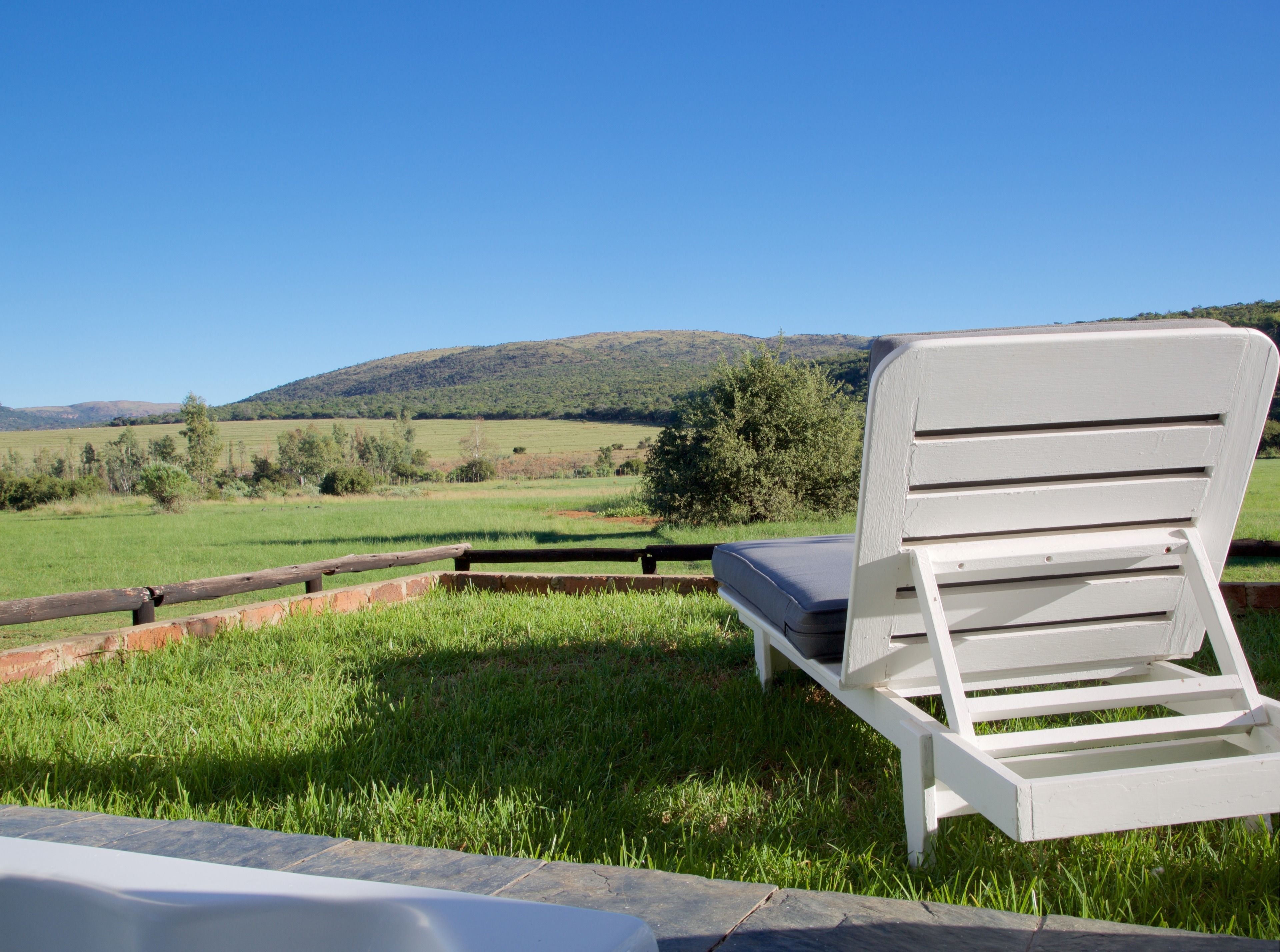 Una silla lounge blanca con cojín en un espacio exterior cubierto de césped, con vistas a un paisaje pintoresco con colinas y árboles.