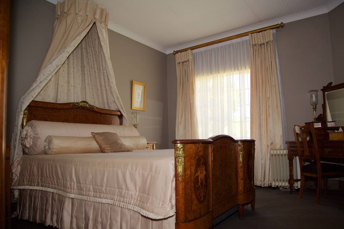 Une chambre à coucher avec un lit à baldaquin, une commode en bois, une table de chevet et un miroir.
