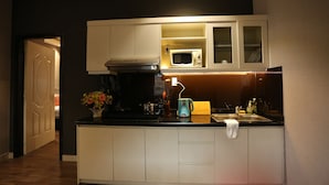 Una cocina compacta con armarios blancos, un microondas, una cafetera y un lavabo.