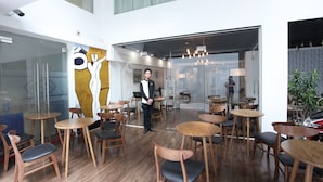 Un café moderno con mesas y sillas de madera, un muro de cristal y un techo con tragaluces.