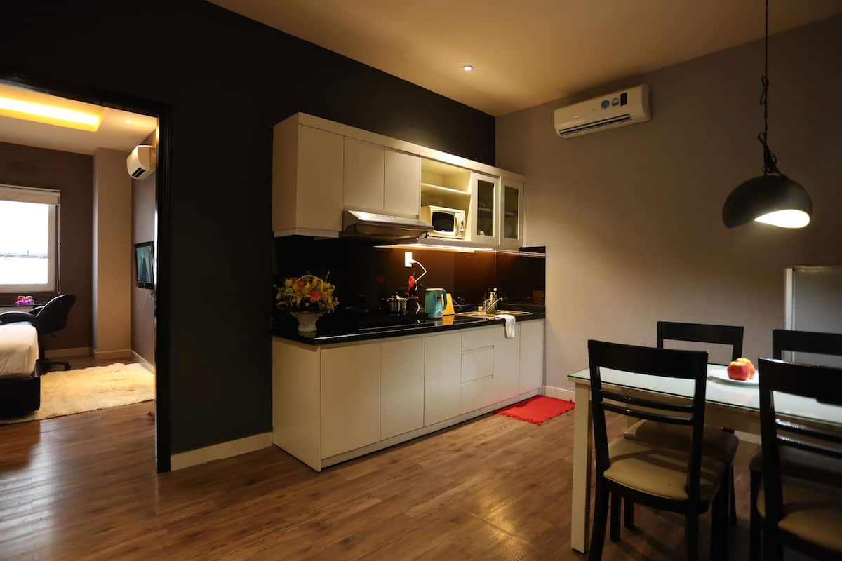 Cocina compacta con armarios blancos, microondas y un lavabo. Hay una mesa de comedor con sillas y una alfombra roja.