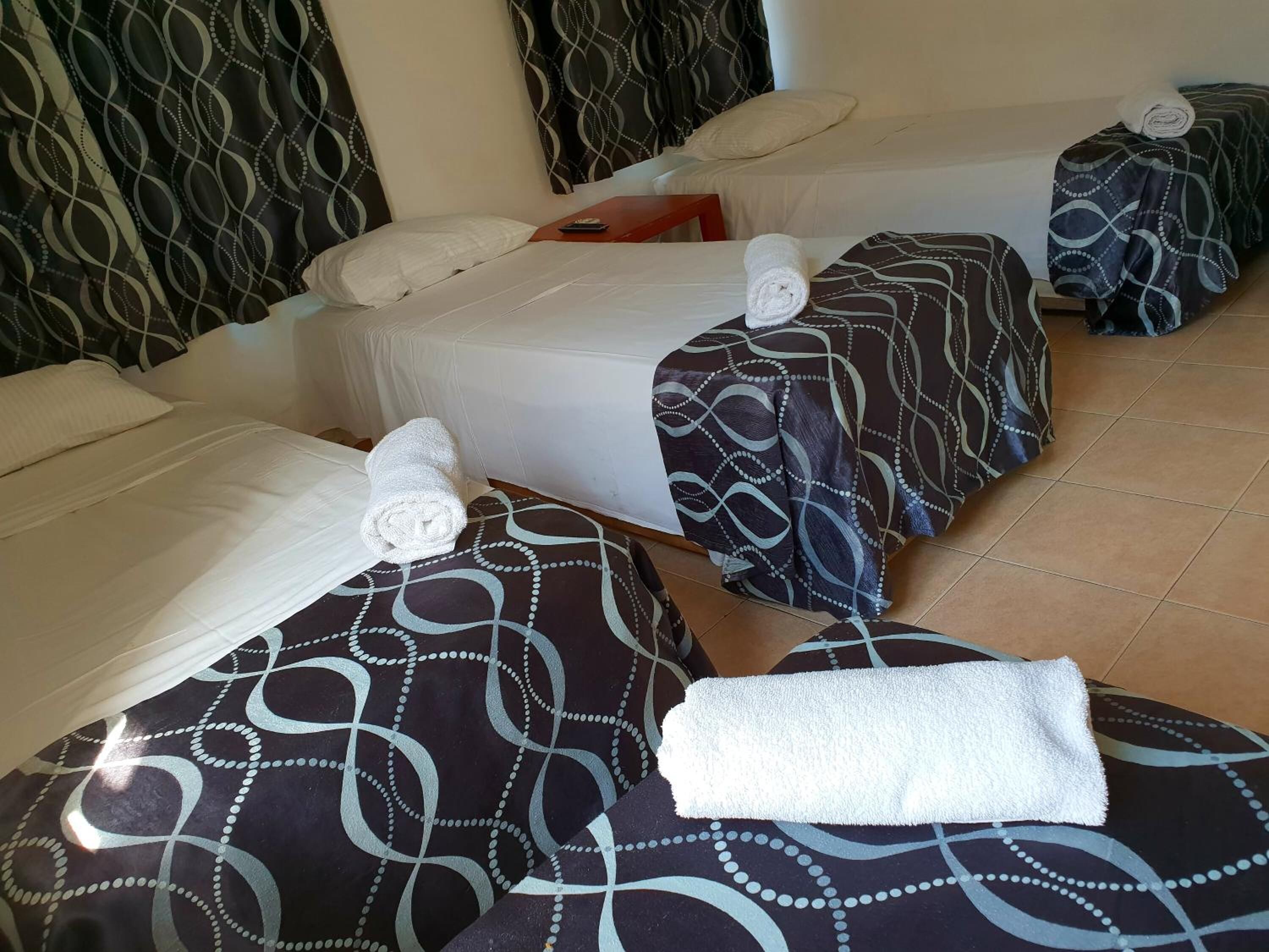 Habitación de hotel con dos camas, cada una con una colcha estampada y una toalla blanca enrollada.