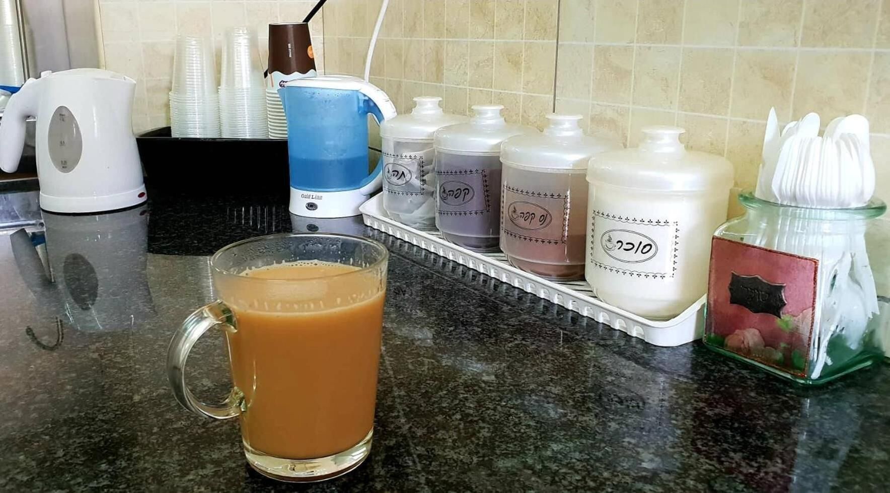 Una encimera de cocina con una cafetera, una taza de café y varios recipientes de condimentos.