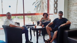 Three people seated in a room with large windows, a small table, and a stone wall. - Atara Hotel (Tiberias)