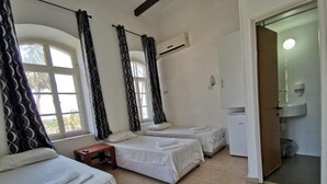 A hotel room with three single beds, a small table, a wardrobe, and a bathroom visible through an open door. - Atara Hotel (Tiberias)