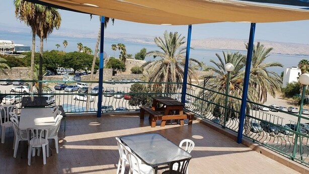 A balcony with outdoor seating, a view of the sea, and parked cars in the background. - Atara Hotel (Tiberias)