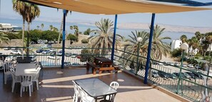 A balcony with outdoor seating, a view of the sea, and parked cars in the background. - Atara Hotel (Tiberias)