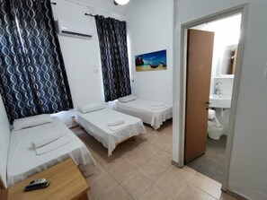 Una habitación de hotel con dos camas individuales, una mesita con un teléfono, un cuadro en la pared y un baño visible a través de una puerta abierta.