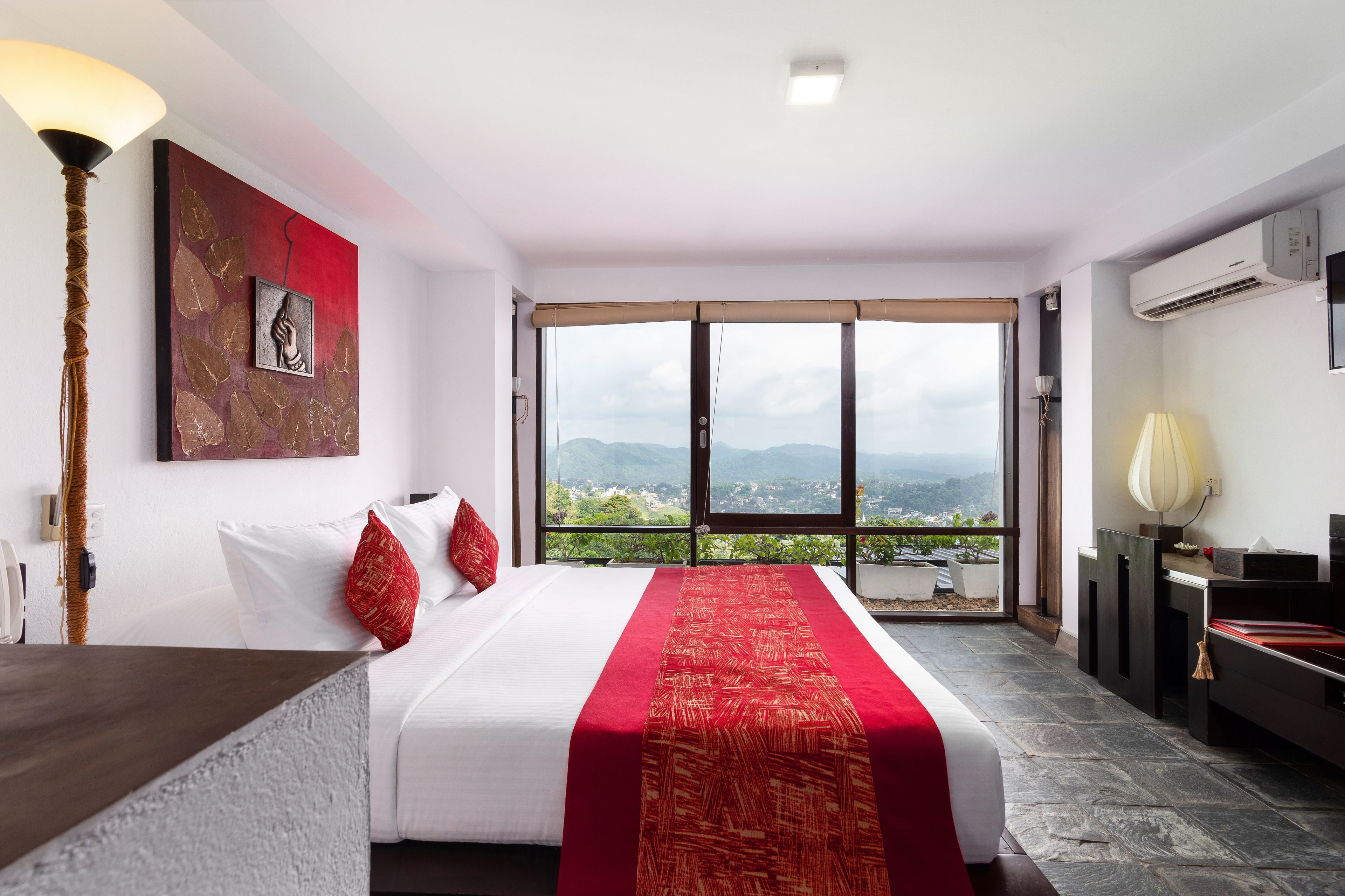 A hotel room with a bed, a view through large windows, and a red decorative item on the bed.