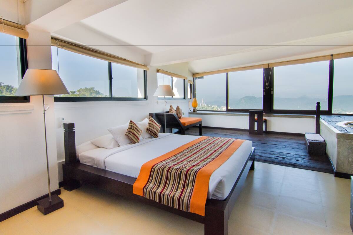 A modern hotel room with a large bed, a desk, and a view of the city.
