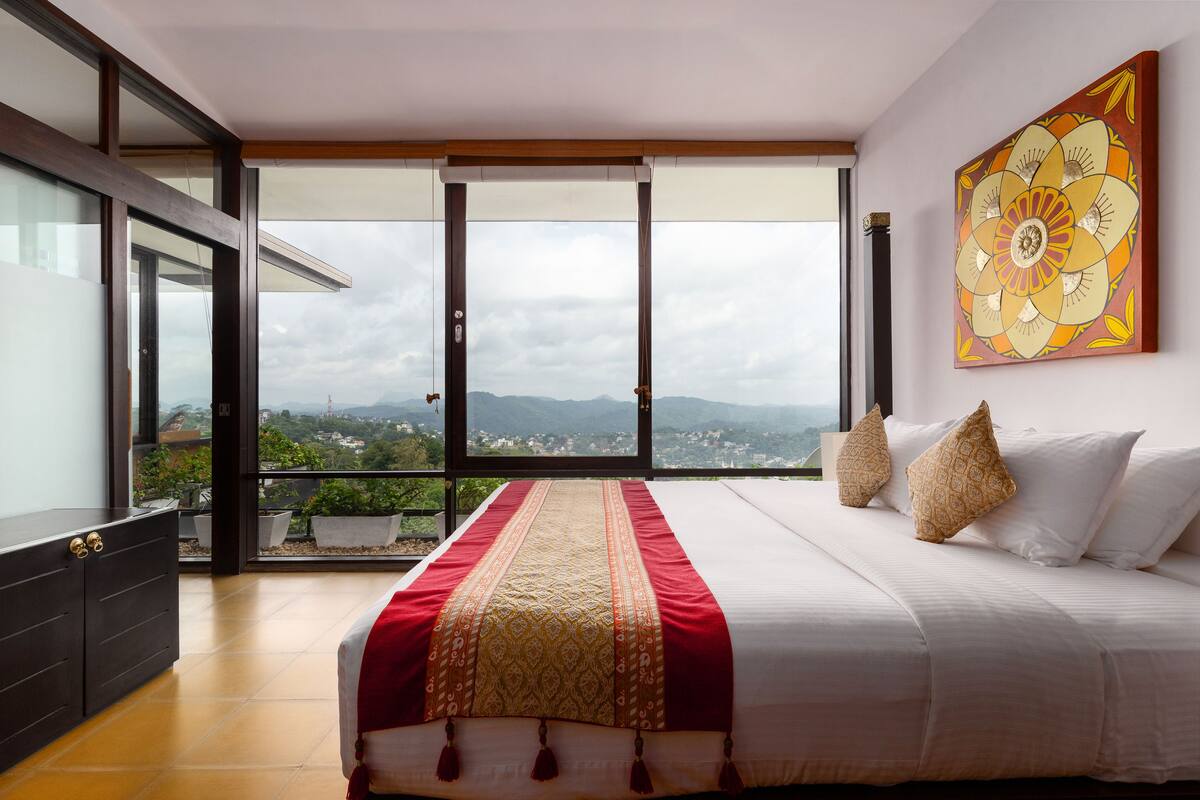 A bedroom with a large bed, a view of the city, and a balcony.