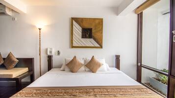 Habitación de hotel con una cama grande, una mesita de noche, una lámpara, teléfono en la pared y una ventana con vistas a zonas verdes.