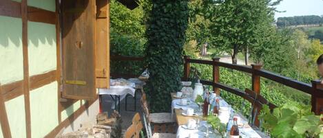 A dining table set outdoors with a view of a vineyard and a building with exposed wooden beams.