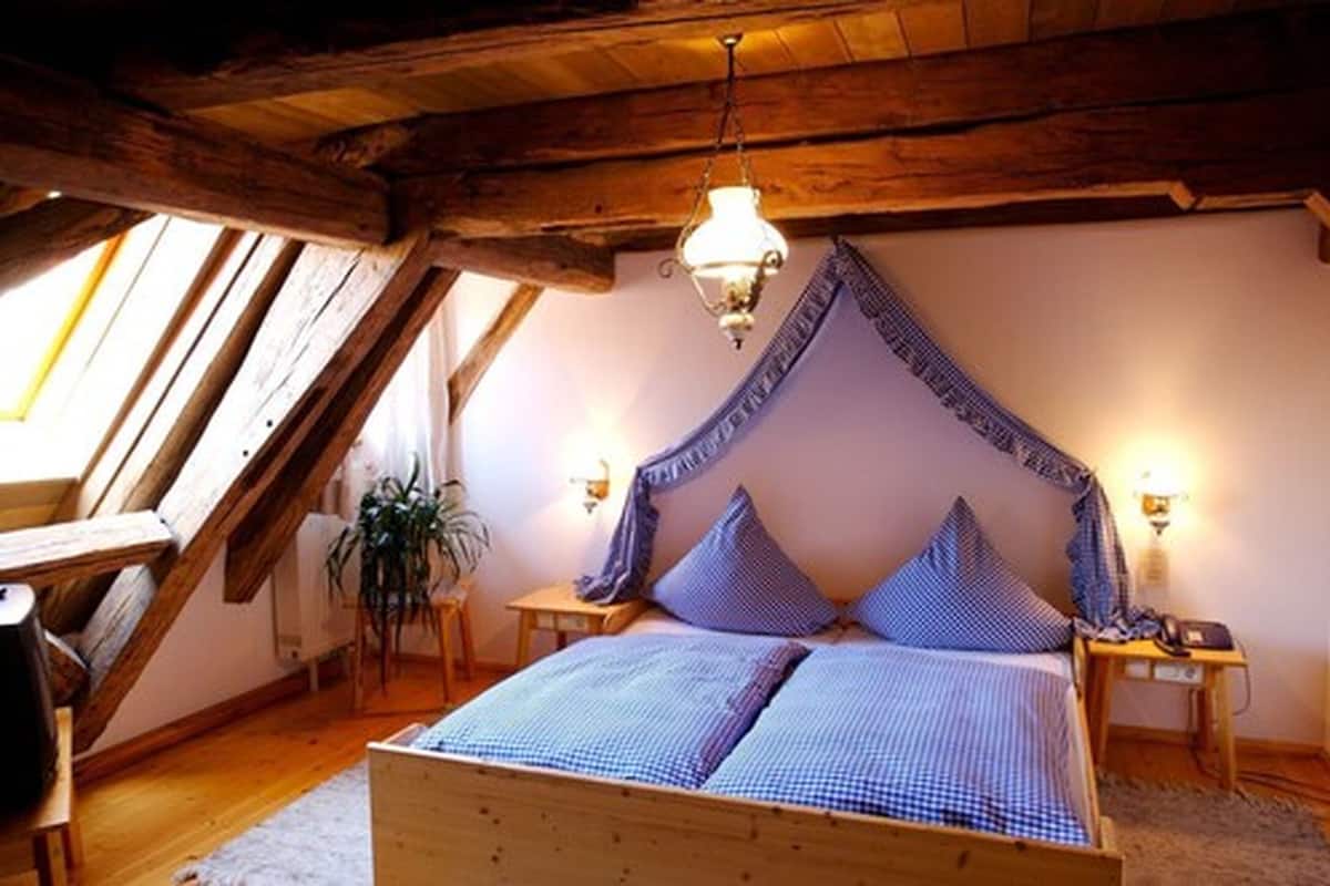 A bedroom with a sloped ceiling, a bed with blue bedding, two bedside tables with lamps, and a window providing natural light.