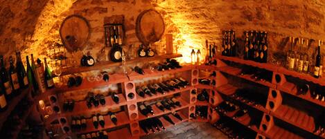 Una bodega subterránea con estanterías de madera que albergan botellas de vino y copas.