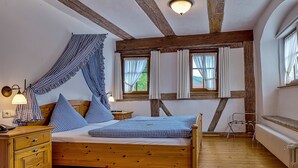 A wooden bed with checkered bedding, a nightstand with a lamp, and a window with curtains. - Landhaus Zum Falken (Adelshofen)
