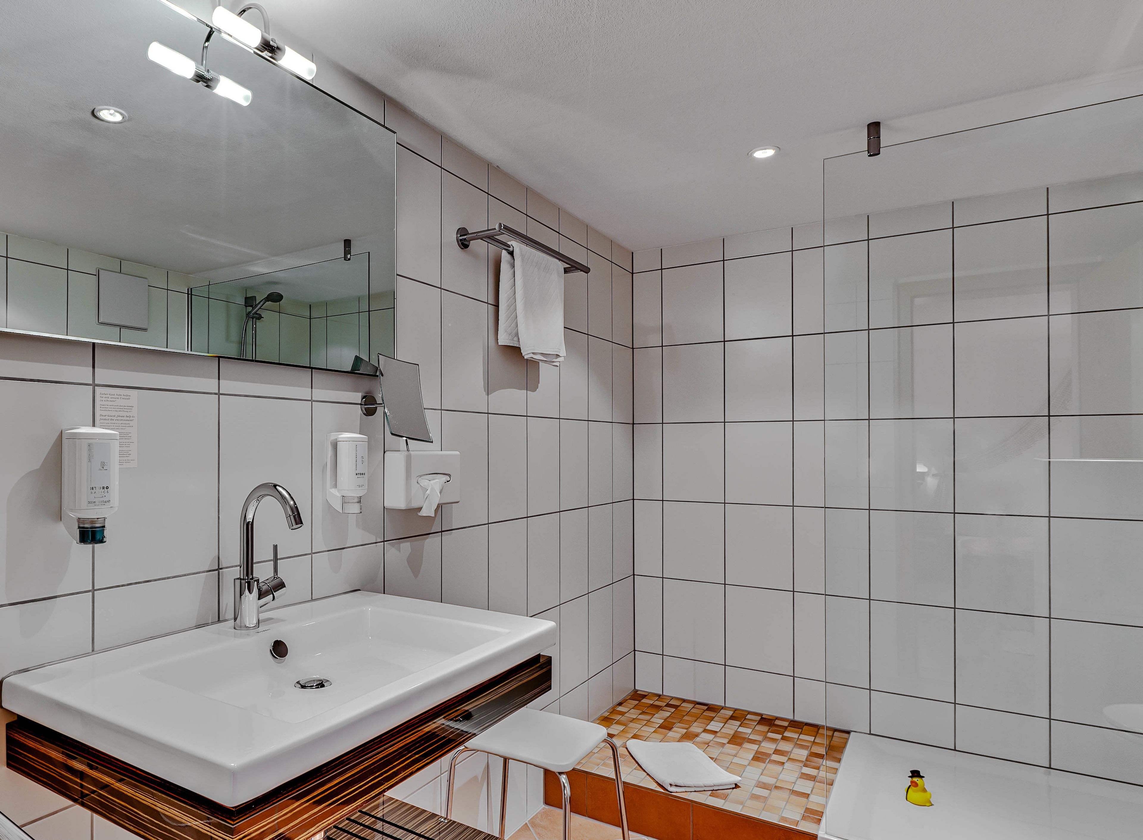 Ein modernes Badezimmer mit einem großen Waschbecken, Spiegel, Handtuchhalter und Dusche.