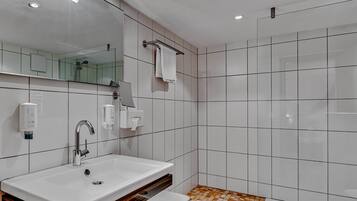 Ein modernes Badezimmer mit einem großen Waschbecken, Spiegel, Handtuchhalter und Dusche.