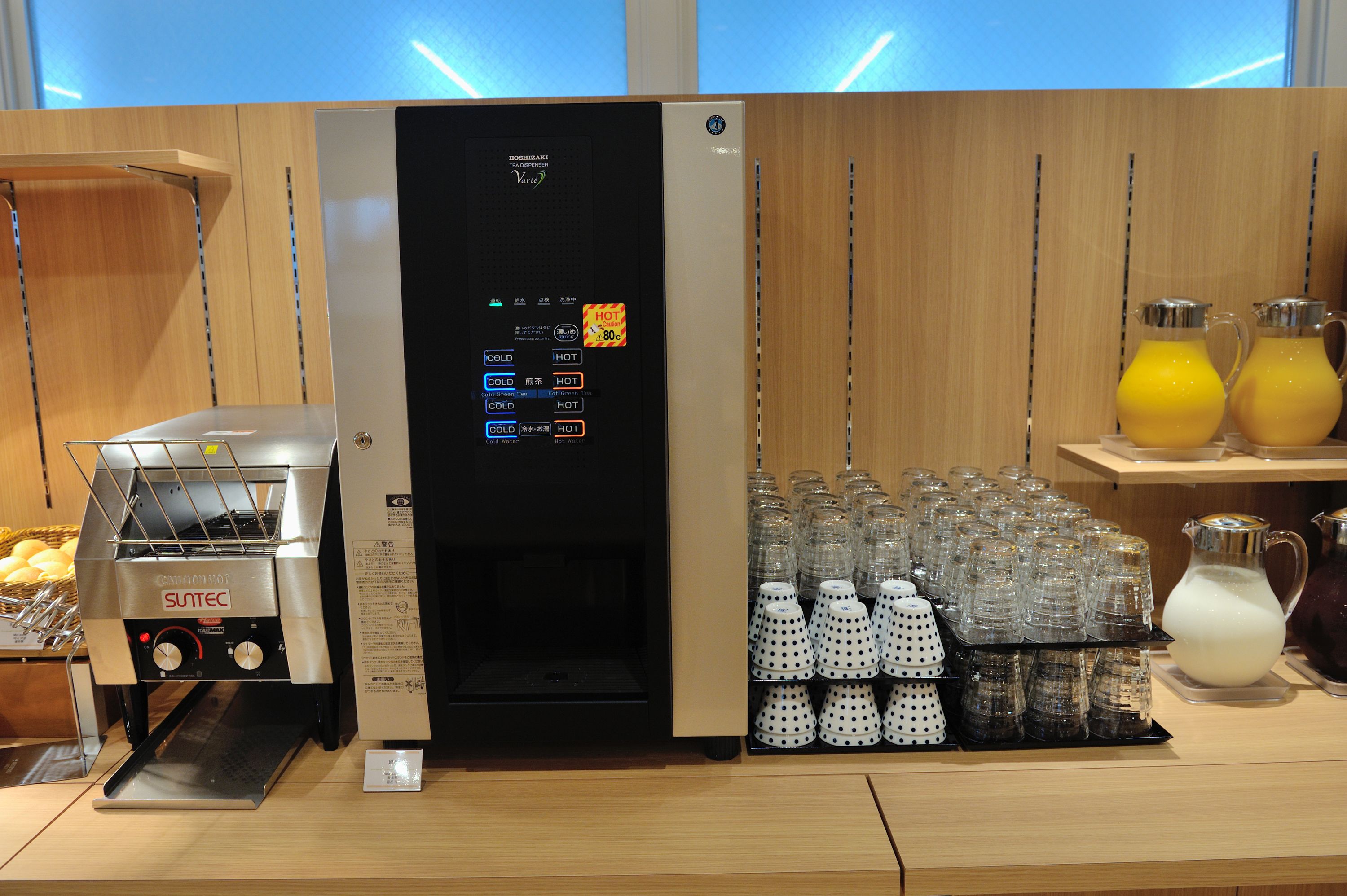 A coffee machine with a digital display, a milk frother, and a variety of glass cups and pitchers on a wooden counter.