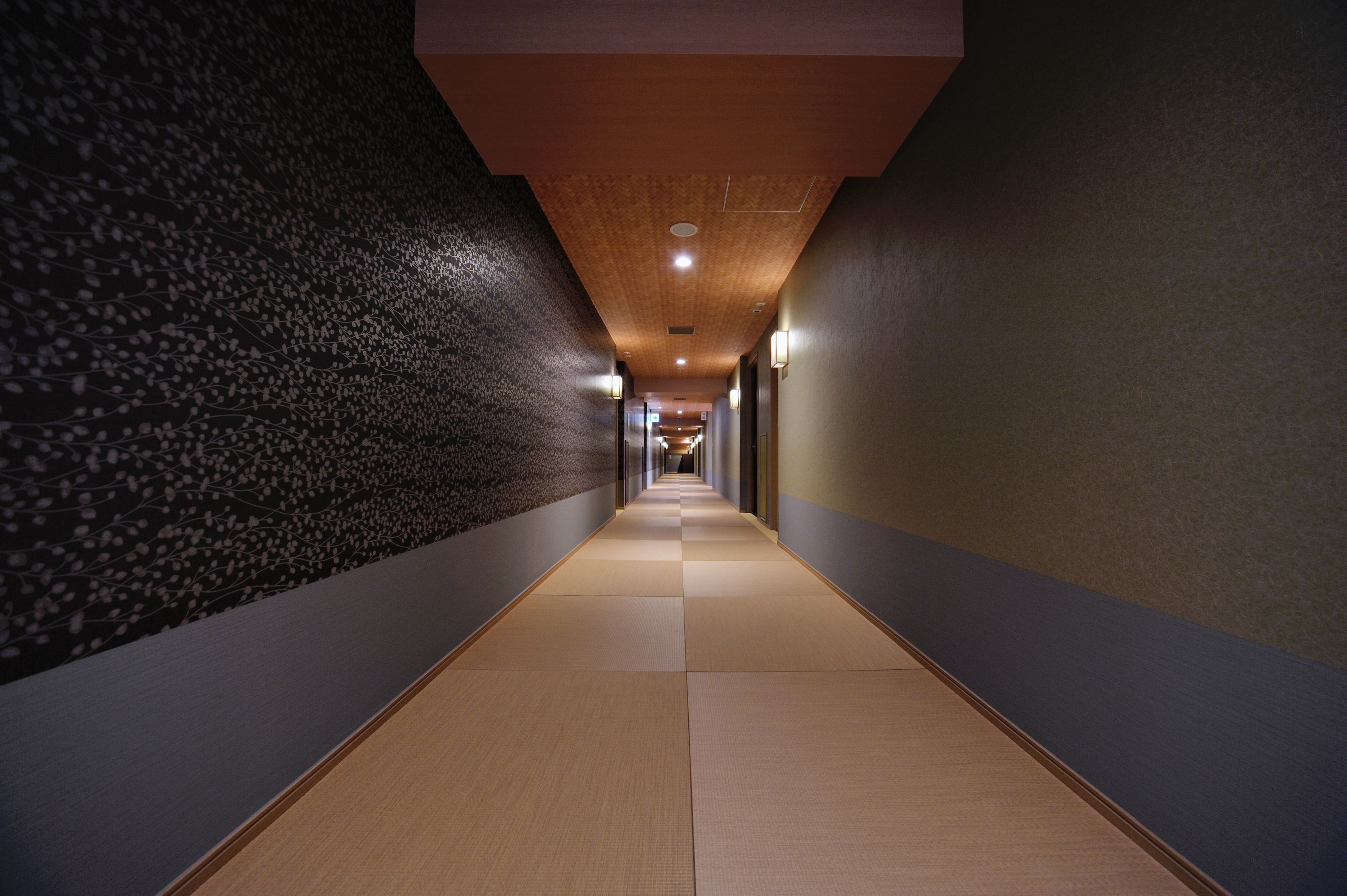 A corridor with tatami mats, a patterned wall, and recessed lighting.