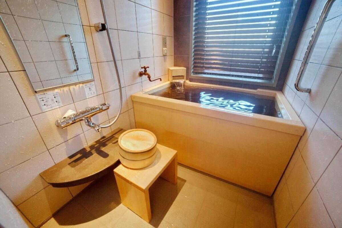 Un baño con bañera, inodoro y ventana con persianas.