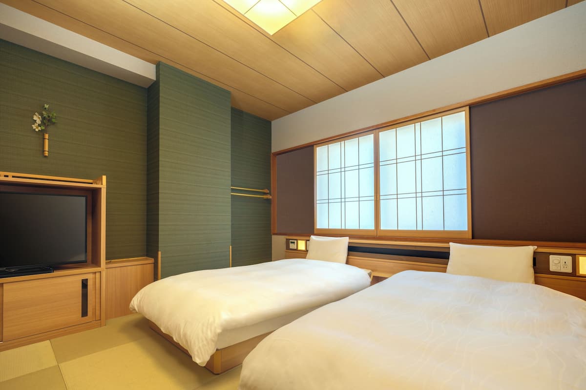 Habitación de hotel con dos camas, un televisor, una ventana y techo de madera.