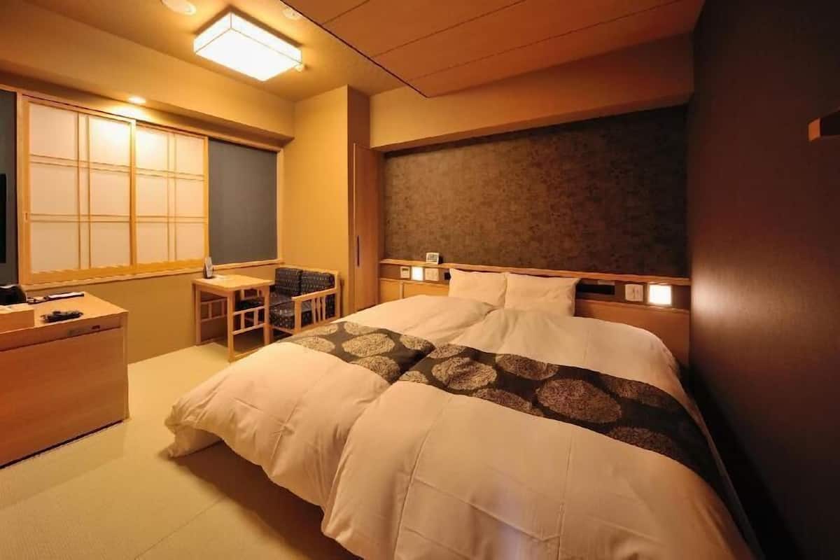 Habitación de hotel con cama, mesita de noche, silla y un ventanal grande con puertas correderas.