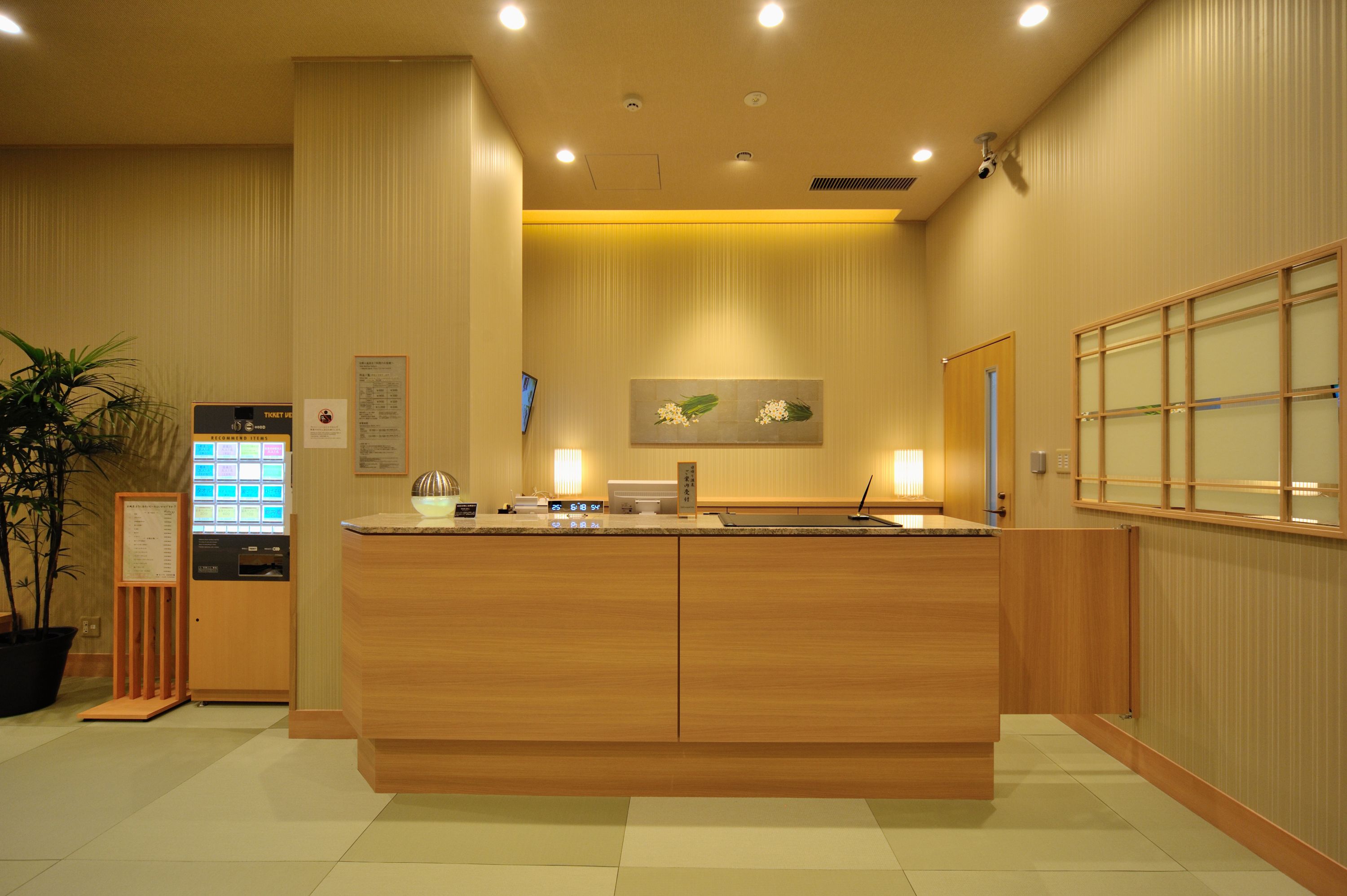 A reception desk with a ticket machine, a potted plant, and a wall-mounted menu board in a hotel lobby.