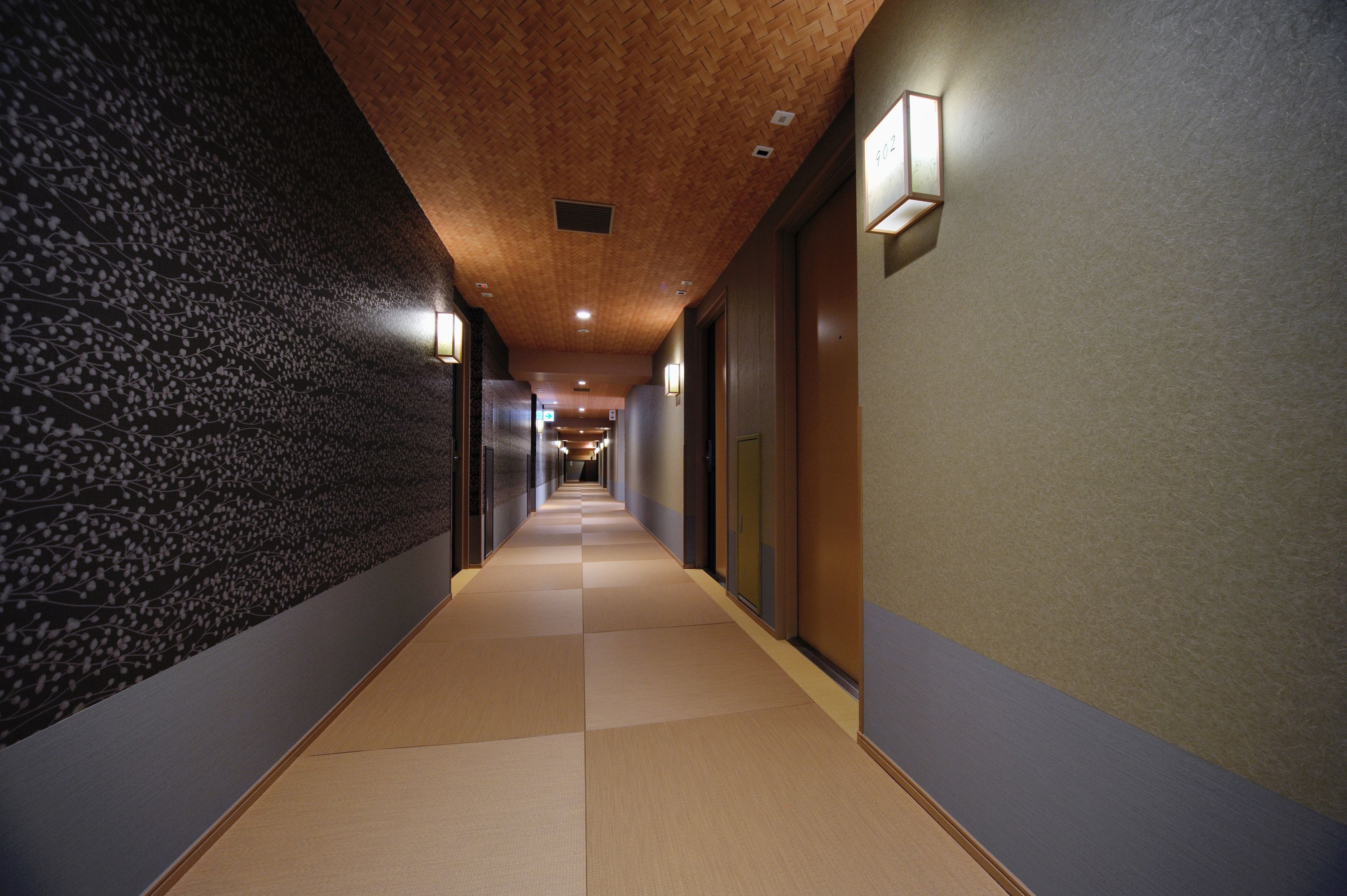 Un couloir avec un mur orné de motifs sur le côté gauche, un plafond en bois et un luminaire sur le côté droit.