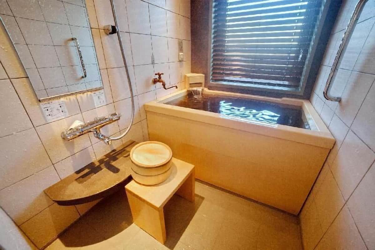 Un baño con bañera, inodoro, ducha y una ventana con persianas.