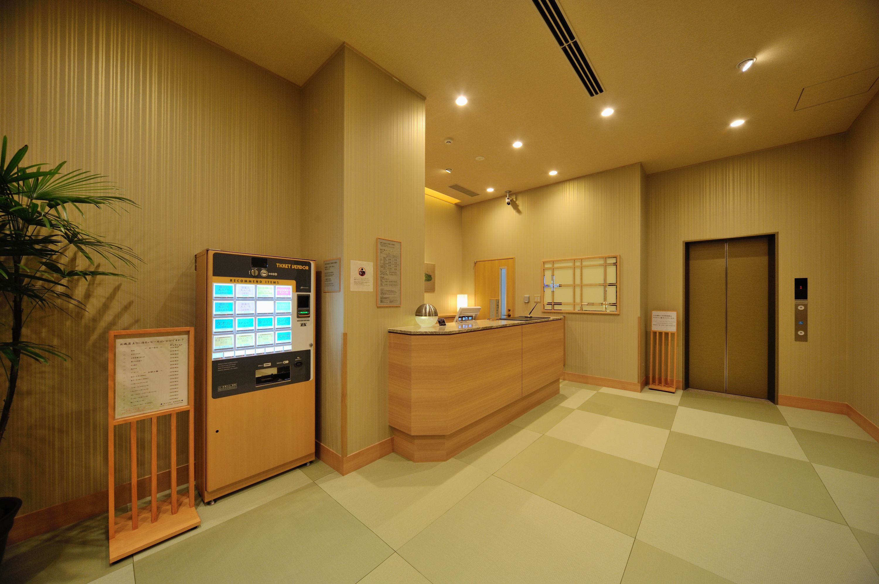 A reception area with a reception desk, a vending machine, a plant, and an elevator.