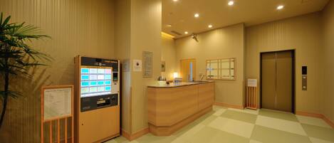 A reception area with a reception desk, a vending machine, a plant, and an elevator.