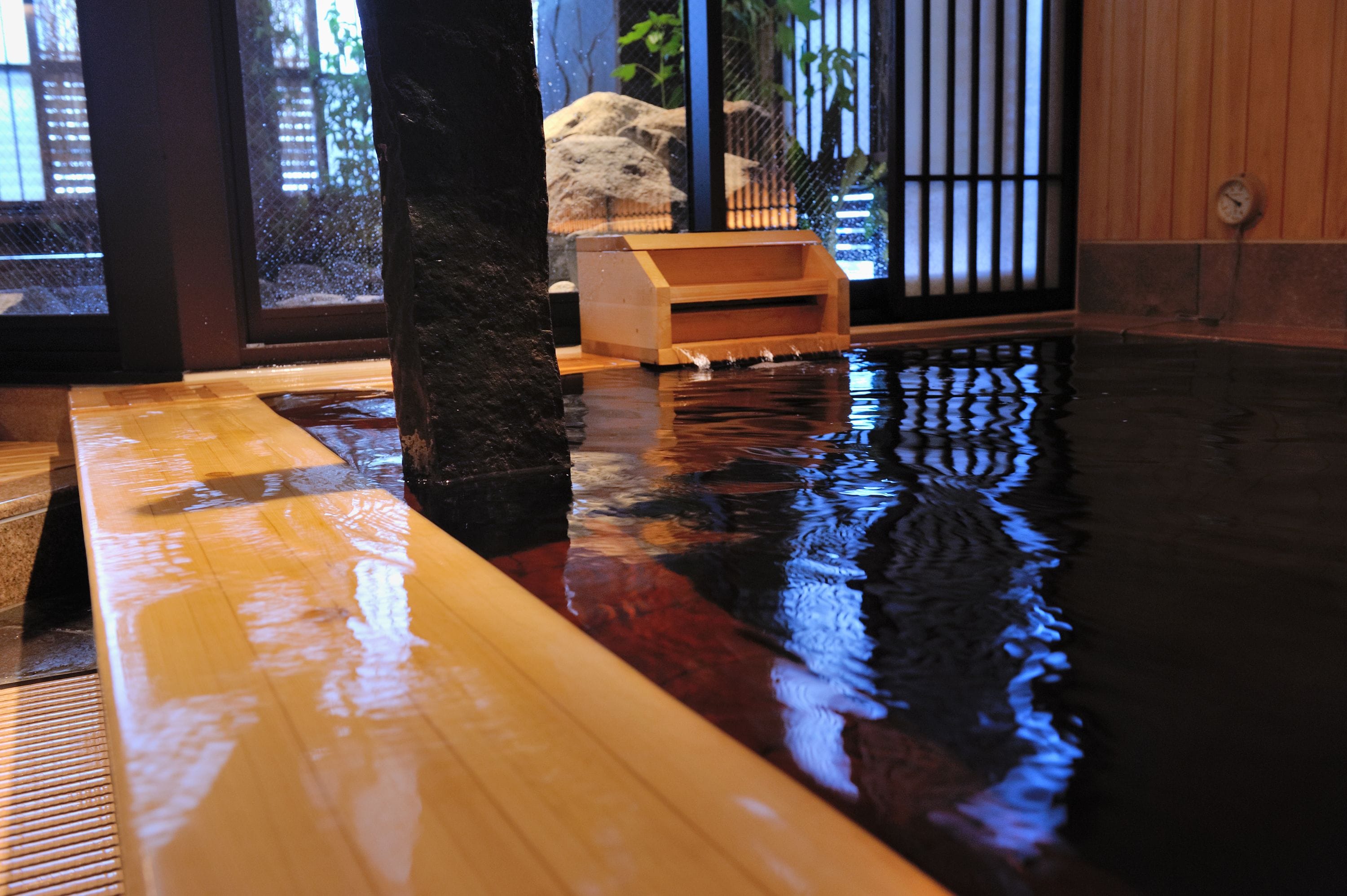 A traditional Japanese onsen with a wooden bench and a stone pillar.