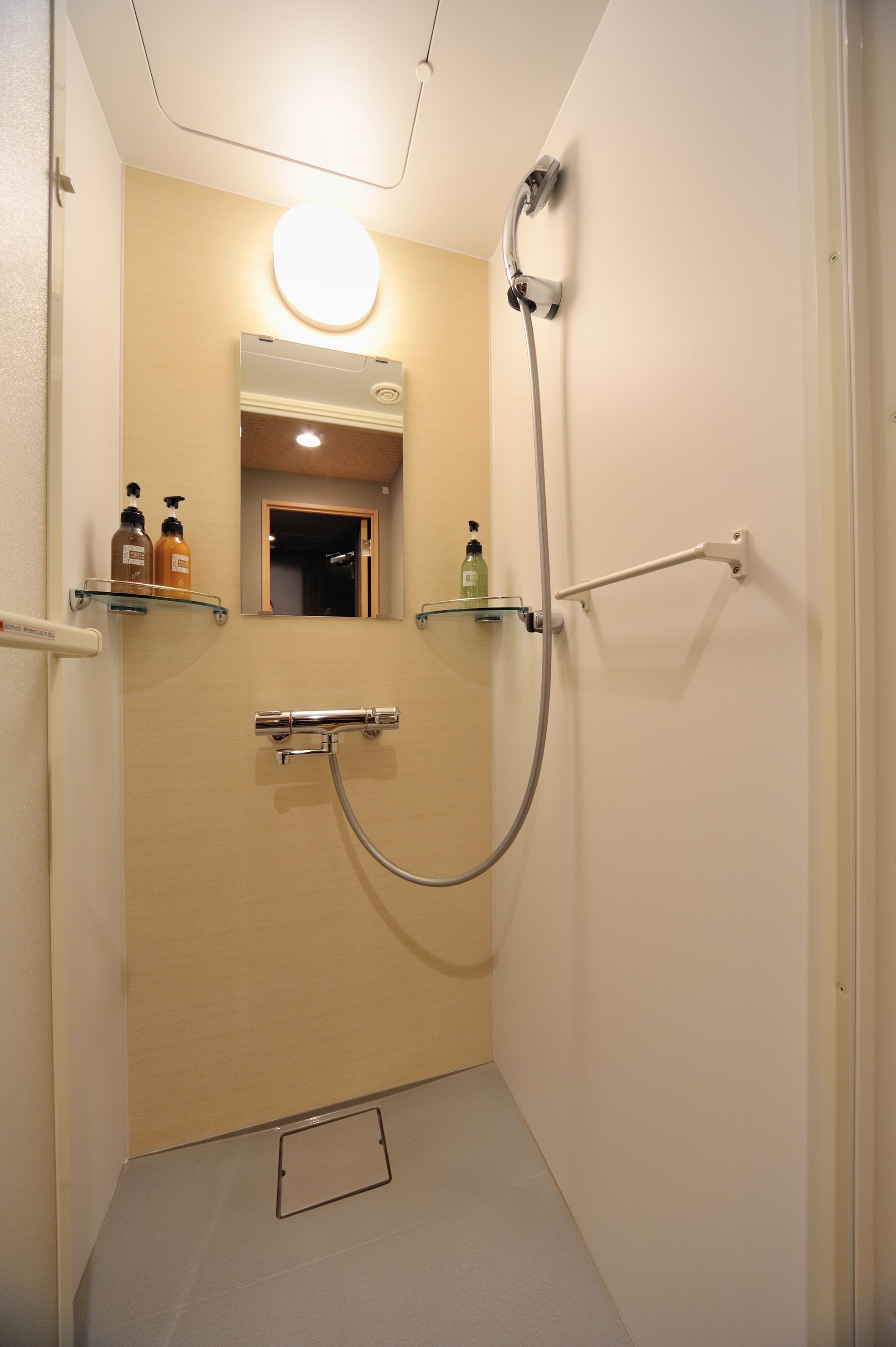 A small, narrow bathroom with a shower, a mirror, and two shelves with toiletries.