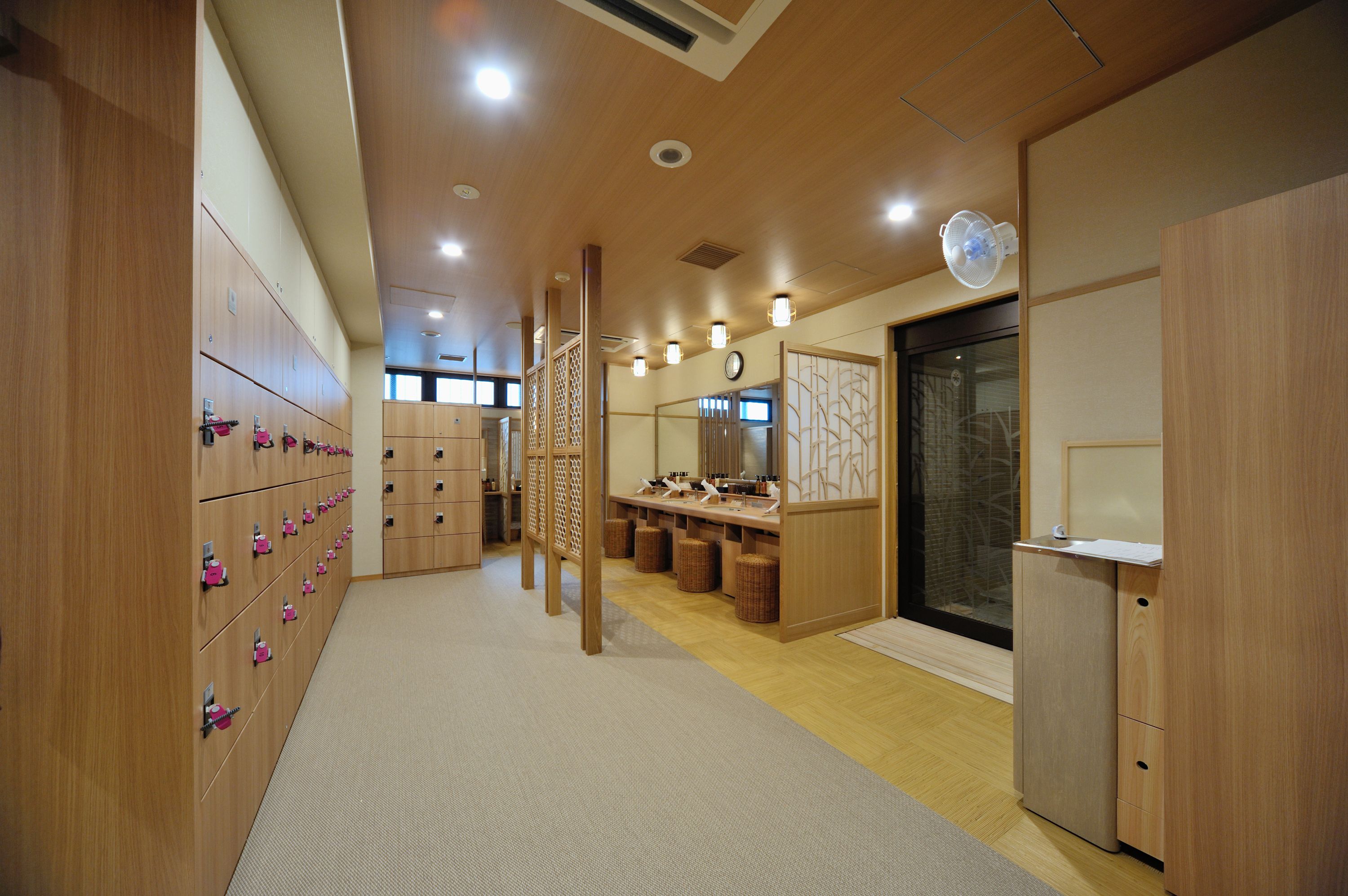 A modern hotel room with wooden lockers, a vanity with a mirror, and a small refrigerator.