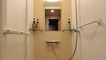 A narrow bathroom with a shower, a toilet, and a small mirror. There are two bottles of soap on a shelf.