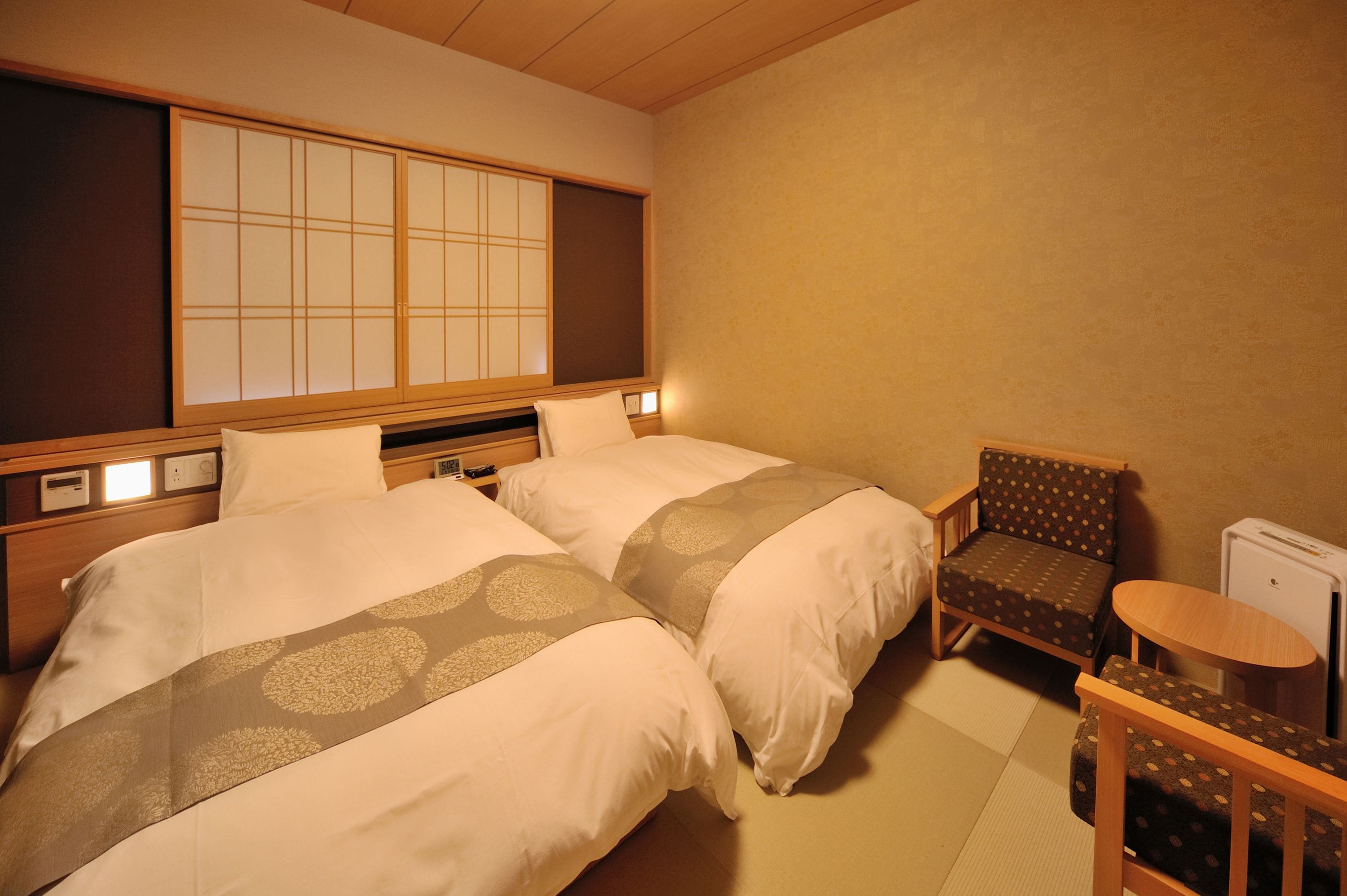 A hotel room with two beds, a traditional Japanese sliding door, a small table, and a chair.