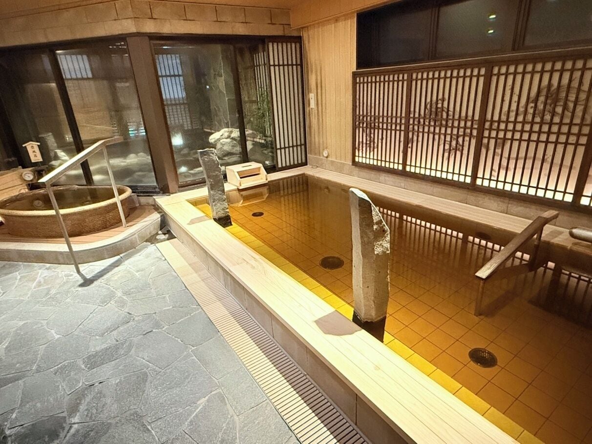 Un onsen japonais traditionnel, avec un sol en pierre, des bancs en bois et un espace de baignade carrelé.